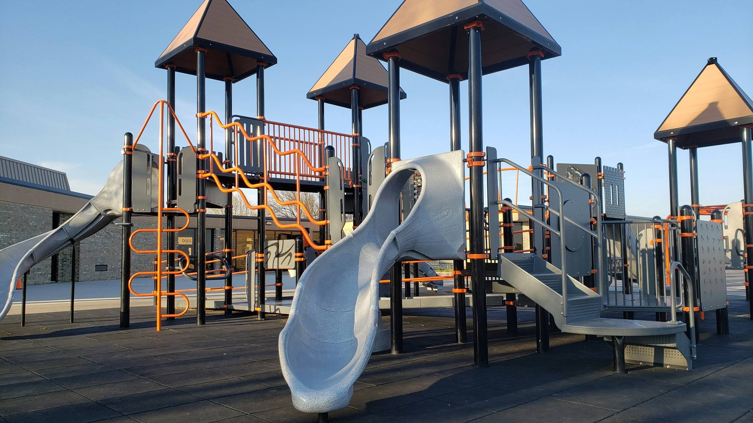 Composite play structure with roofed towers, a stainless steel slide, and climbing elements on a clear day