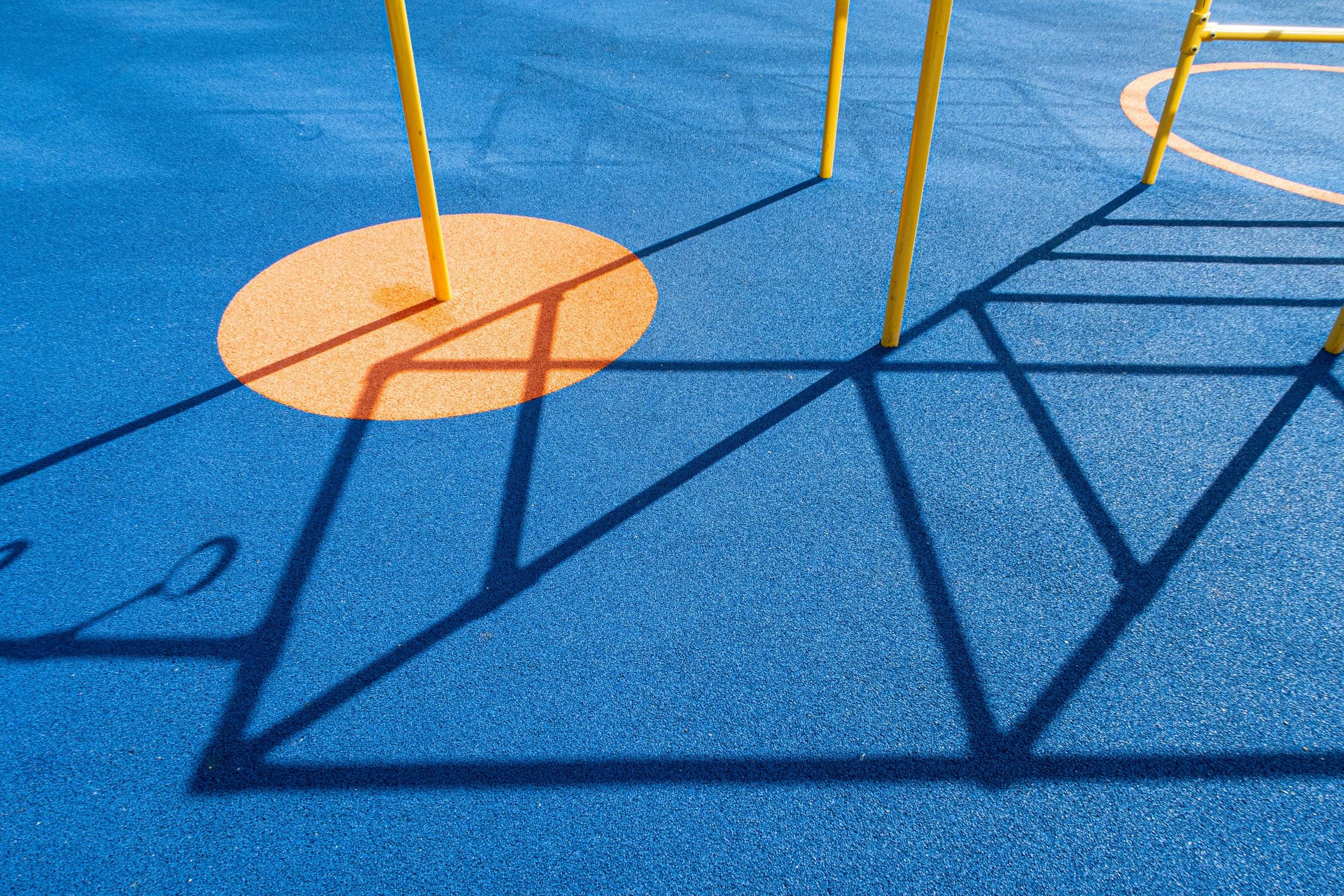 Blue poured-in-place rubber safety surfacing with an orange inlaid circle and the shadows of play equipment